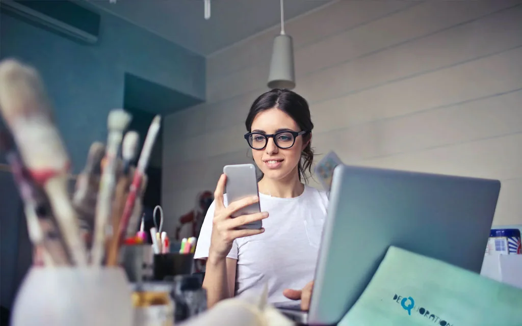 Woman reviewing her phone at a creative desk while consolidating her debt into one payment